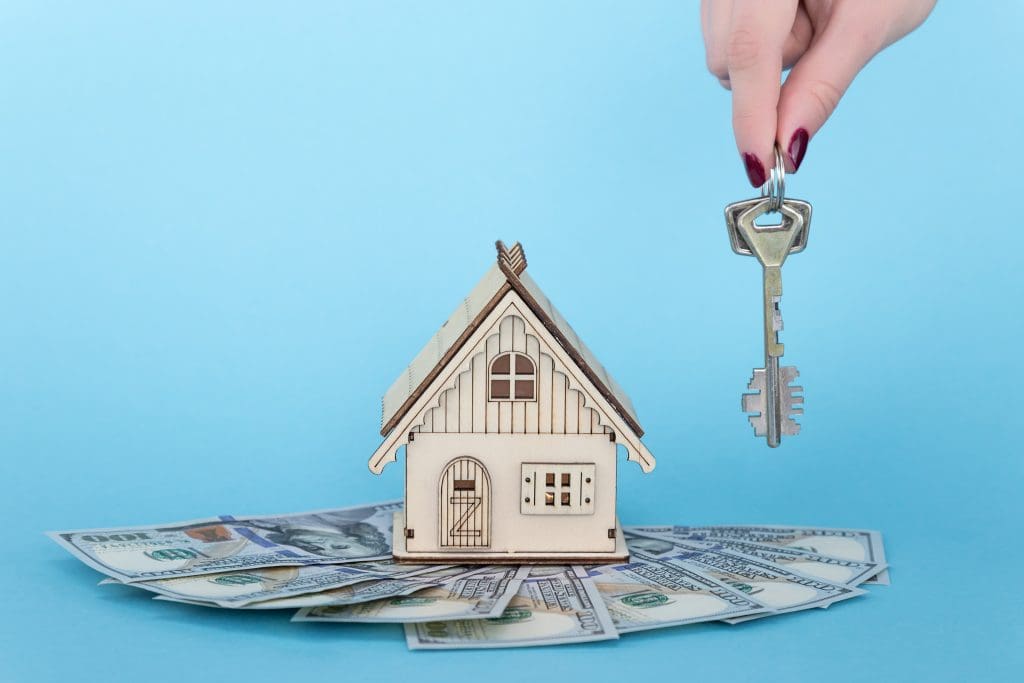 How to market and sell your flipped house. Miniature house sitting on top of money with woman holding keys