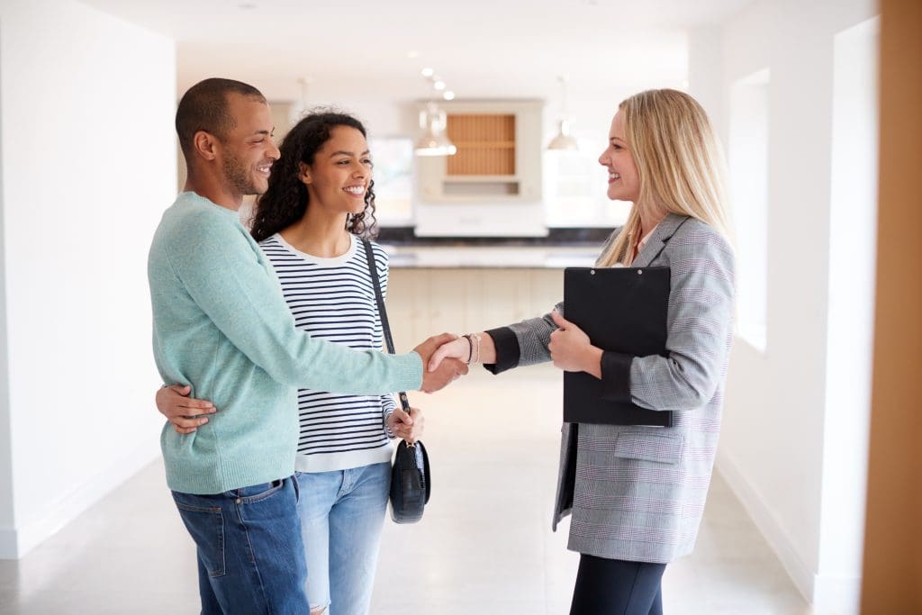 Female Realtor Shaking Hands With Couple.  Pricing your home for maximum profit.