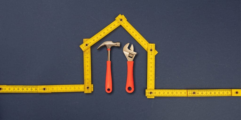 Home repair. Hand tools under house shape yellow wooden measure, blue background. Folding ruler and hardware, workshop, construction, renovation concept.