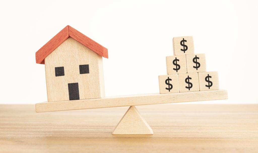 House or Property investment concept. House model and wooden blocks with dollar sign balancing on a seesaw