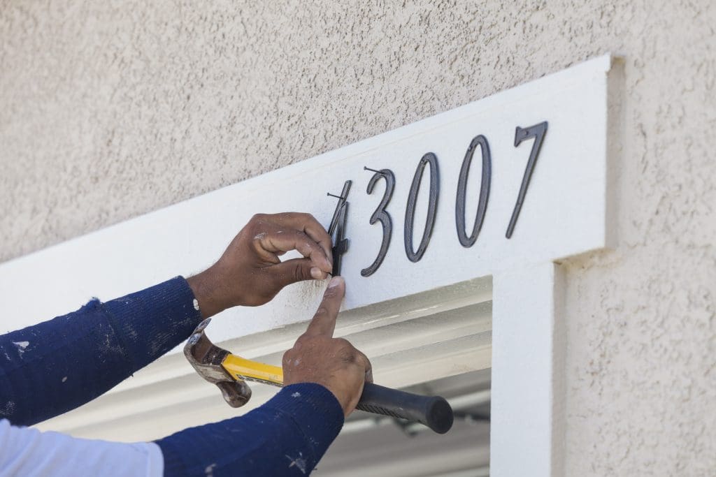 Man Nails Address Numbers onto House Facade.