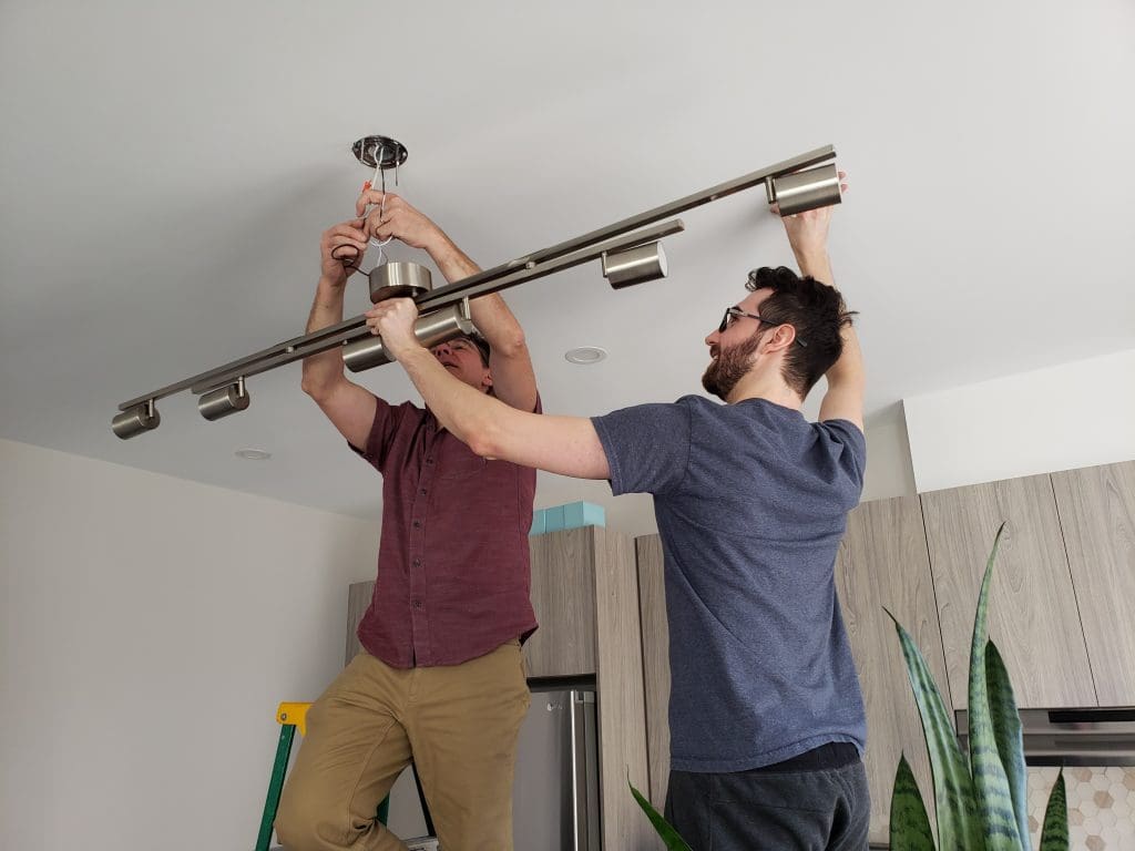 Two men installing a ceiling light fixture. 