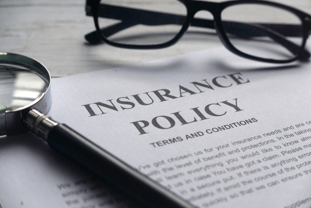  Insurance policy with magnifying glass.  Deciding if you should include insurance and taxes in your mortgage payment. 