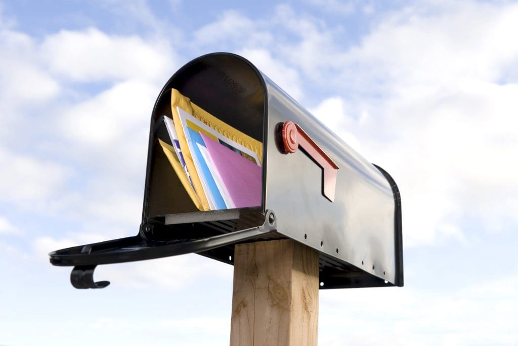 A mailbox full of mail against a blue and puffy white cloud sky