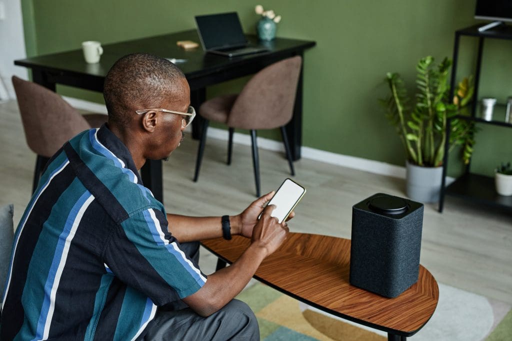 High angle view of man connecting phone to smart speaker with voice controlled home AI