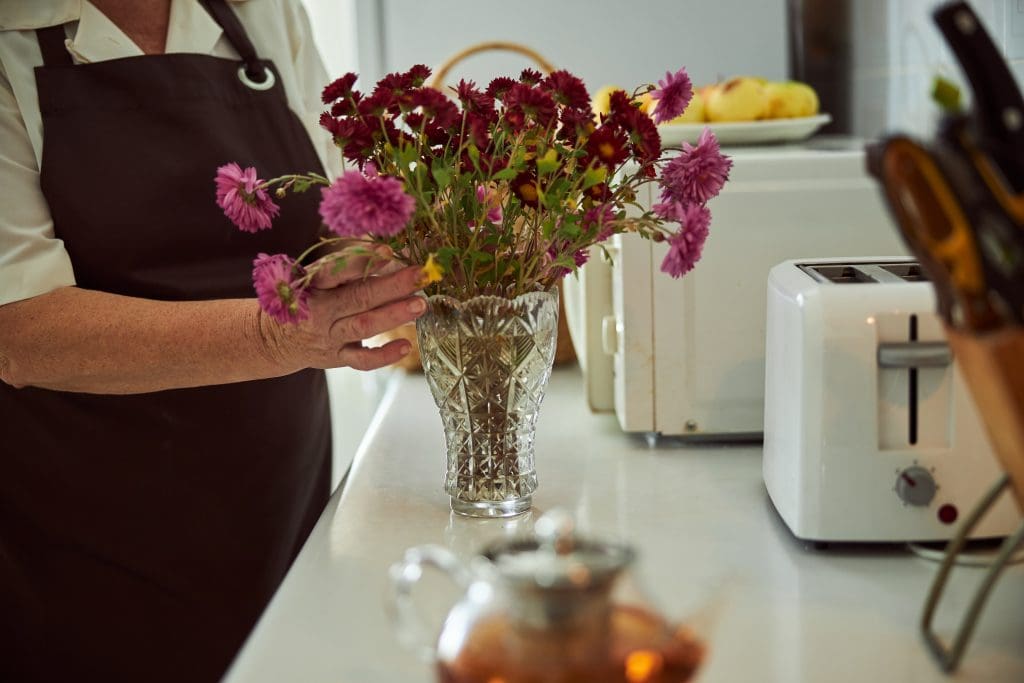 woman wearing an apron arranging flowers in a crystal vase