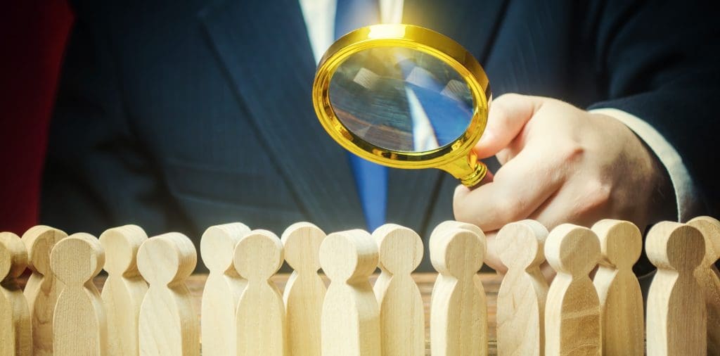 How to Find the Best Mortgage Lender.  Man examining wooden people with magnifying glass.