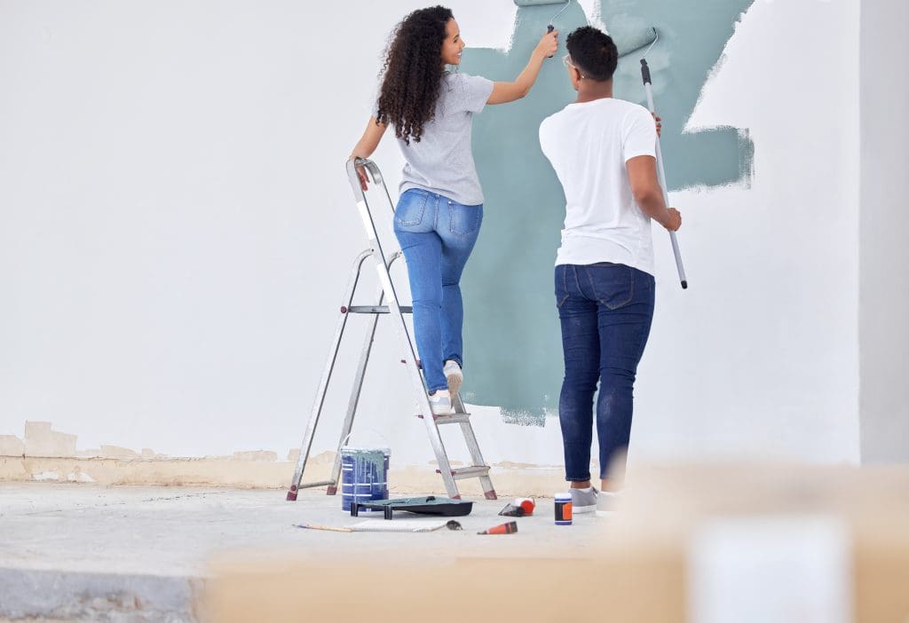 a young couple painting a wall in a room together.