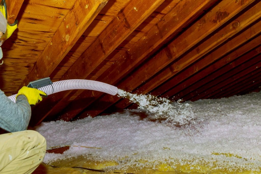 Technician spraying blown Fiberglass Insulation between Attic Trusses 