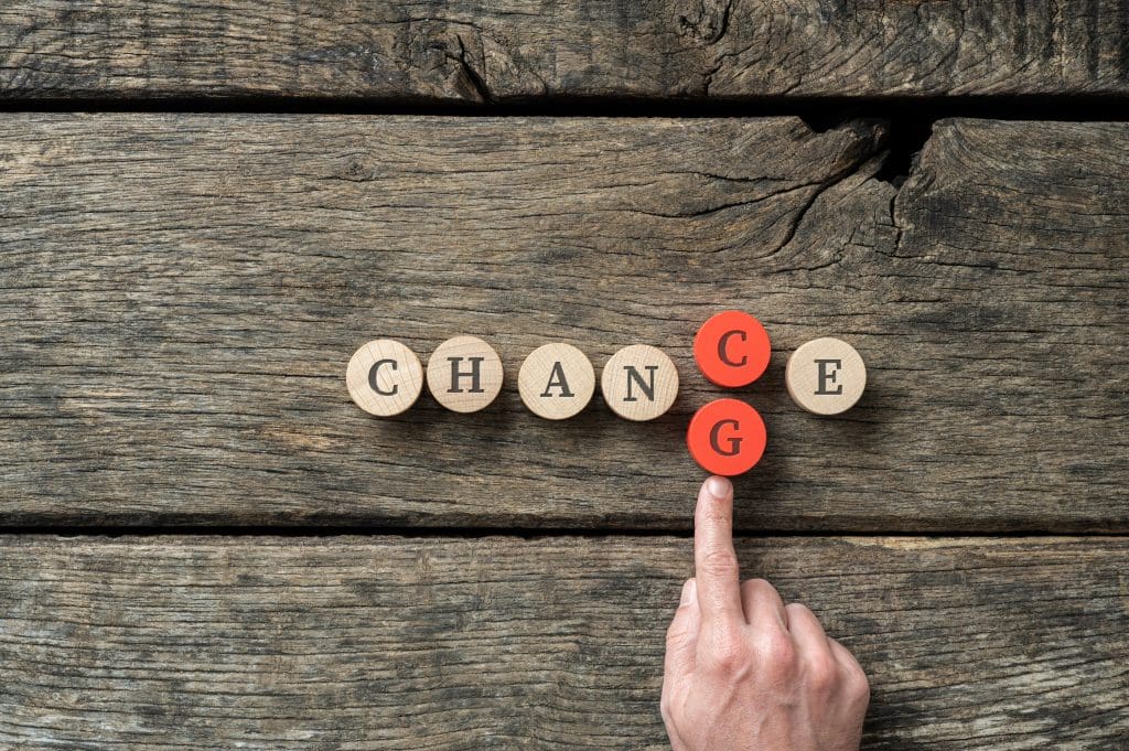 Word Chance spelled on wooden cut circles with male hand pushing in letter G to change it into Change.