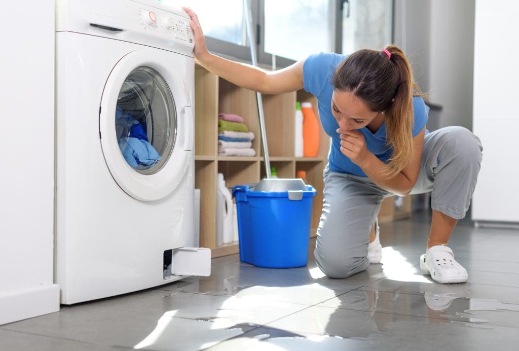 Pensive woman checking a water leak on the floor, the washing machine is broken