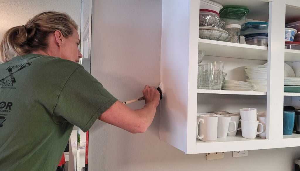 Woman in work clothes painting kitchen cabinet