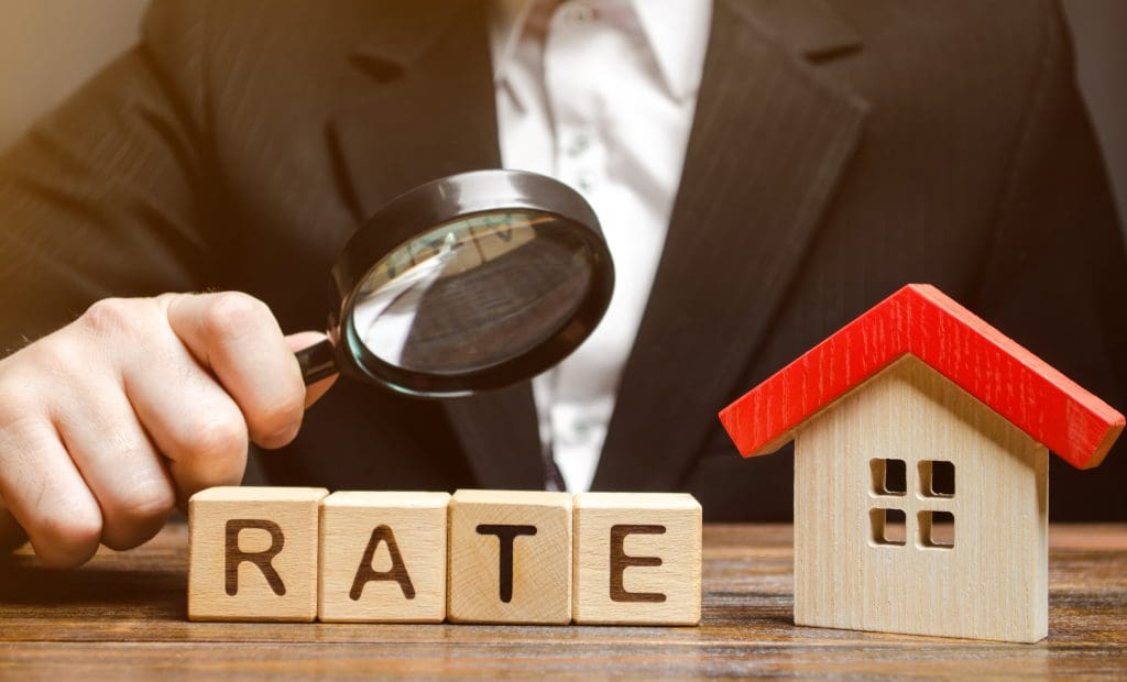 Wooden blocks with the word Rate, house and a magnifying glass in the hand of a man.