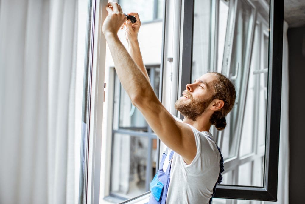 Workman in overalls installing or adjusting plastic windows in the living room at home