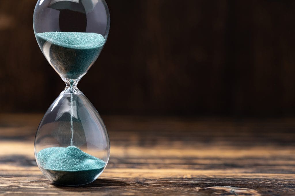 Selective focus of hourglass with green sand on wooden background