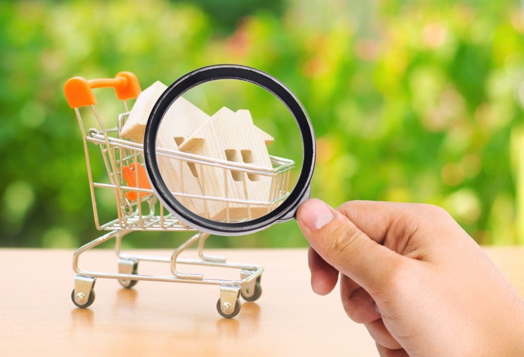 A magnifying glass looks at a wooden house in a trading cart on nature background. 