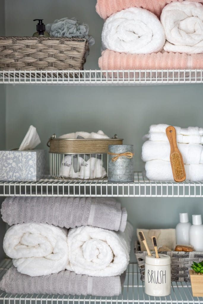 Neatly organized bathroom linen closet with bamboo toothbrushes and gray and white towels
