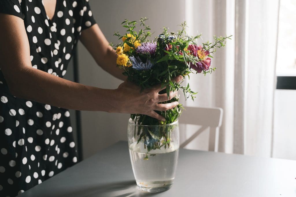 young woman with black dress and white polka dots arranging a bouquet of freshly picked flowers in a glass vase 