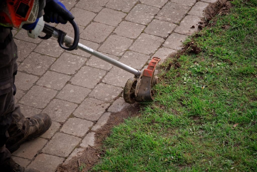 Garden maintenance worker uses an edge trimmer at the sidewalk